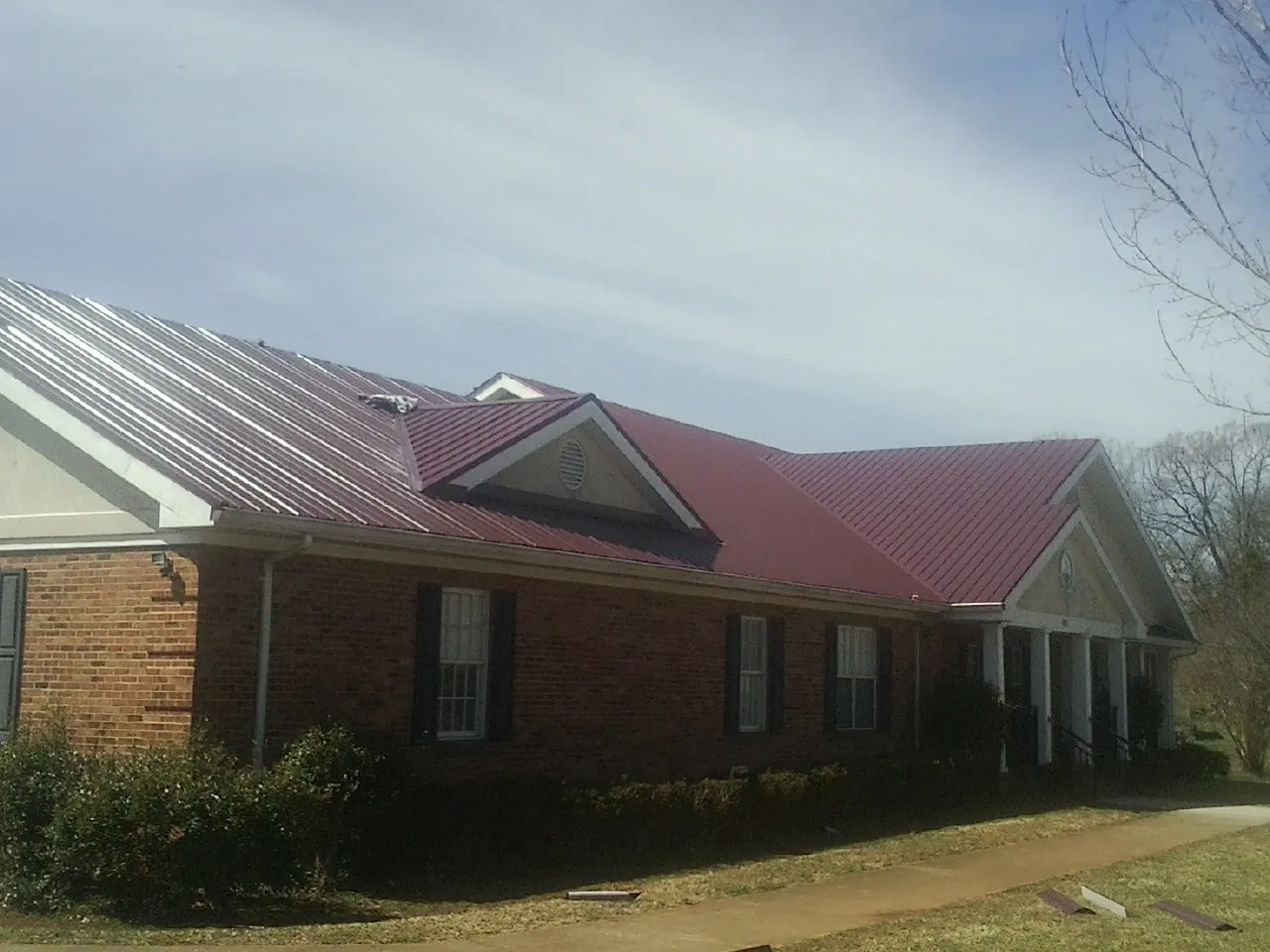 Red metal roof with gabled entries on a long brick building, from a Hail Damage Roof Repair job in Jersey