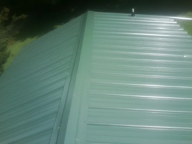 New green metal panels meeting at the ridge of a roof — Flat Roof Repair work by our crew in Jersey